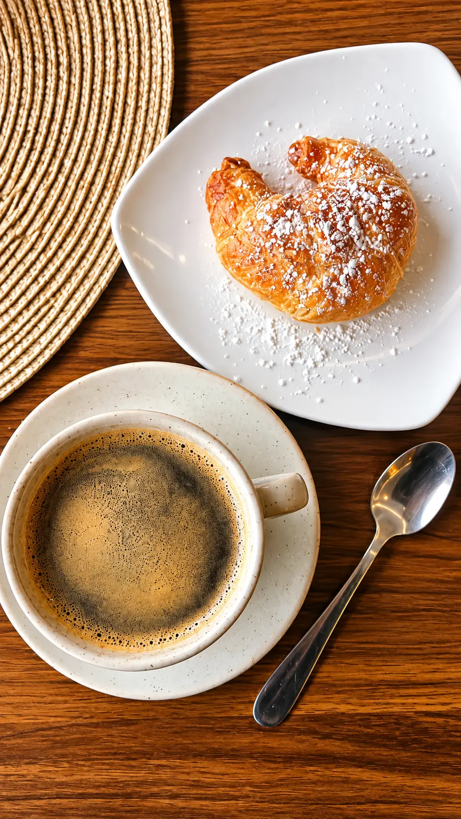 Café y croissant con azúcar glass en una mesa de Vilastrani